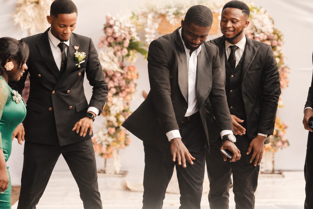 Groomsmen in dark suits dancing together in front of a floral arch